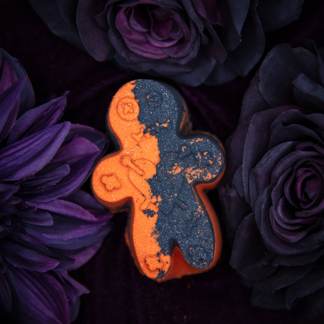 Black and Orange Gingerbread man cookie bath bomb on purple flowers