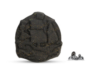 A black bath bomb with gold glitter, designed to resemble a pirate ship, with a small silver pirate ring beside it.